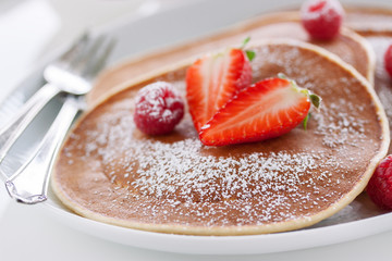 Homemade buttermilk american pancakes with fresh strawberry and raspberry on a white plate on a white table for breakfast, closeup, selective focus..