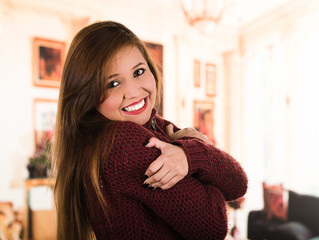 Pretty young brunette woman wearing red sweater, rubbing shoulders as being cold