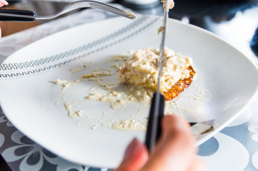 Closeup white plate with creamy dinner dish on top, knife and fork cutting into food