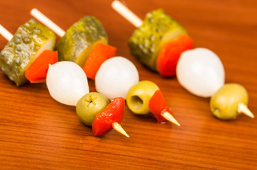 Vegetable skewers of pickles, olives, capiscum and baby onions lying on wooden surface as seen from above