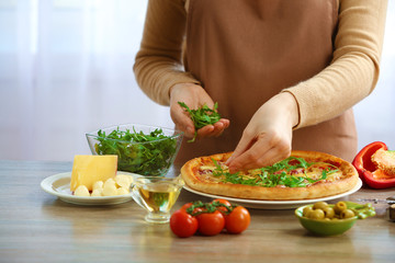 Woman decorating fresh baked pizza with arugula, close up
