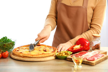 Woman cutting fresh baked pizza, close up