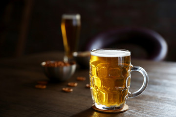 Glass mug of light beer with snacks on wooden table