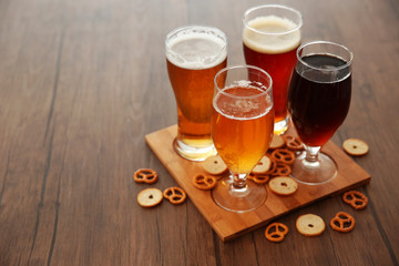 Glasses with different sorts of craft beer and snacks on wooden tray