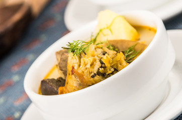 Classy serving of potato soup with meat and vegatables, served in white bowls sitting on table, blue tablecloth, cozy restaurant background