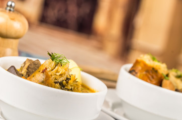 Classy serving of potato soup with meat and vegatables, served in white bowls sitting on table, blue tablecloth, cozy restaurant background