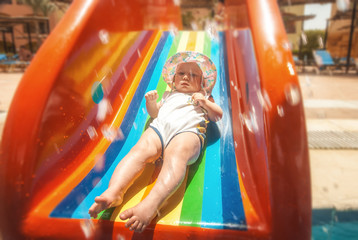 Fototapeta na wymiar Little baby on a rainbow slide in aquapark