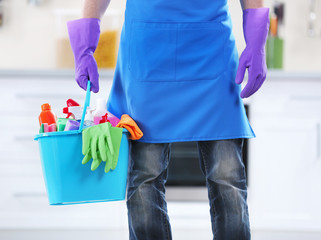 Man holding plastic bucket with brushes, gloves and detergents in the kitchen