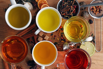 Cups with different kinds of tea and ingredients on table