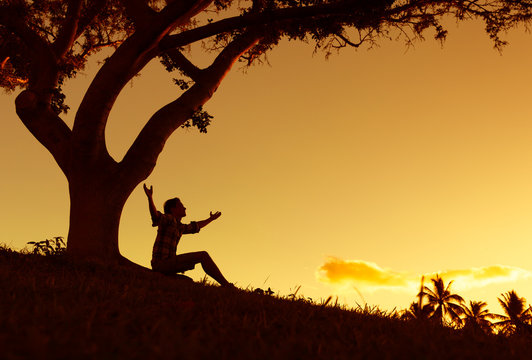 Happy young man outdoors with arms up in the air looking at the sunset. 