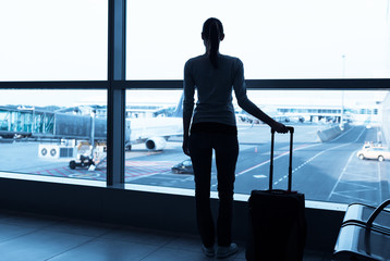 Young woman in the airport, looking through the window at planes