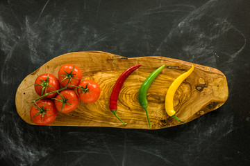 Tomatoes and chili peppers on wooden board.