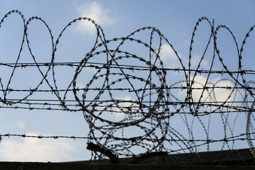 Prison wall barbed wire fence detail with blue sky in background