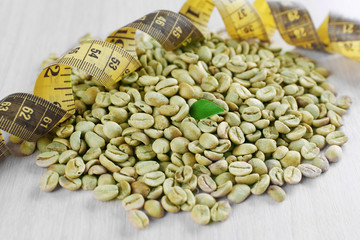 Green coffee beans with measuring tape on white wooden table