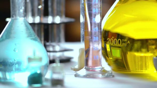 Flasks with yellow and blue reagents, test tubes and beakers in a chemical laboratory,  blurred background, filmed on telephoto lens