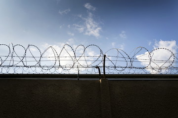 Prison wall barbed wire fence detail with blue sky in background