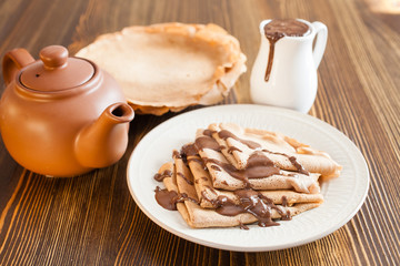 the chocolate pancakes watered with chocolate sauce in a plate on a table, selective focus