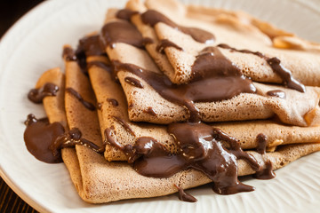 the chocolate pancakes watered with chocolate sauce in a plate on a table, selective focus