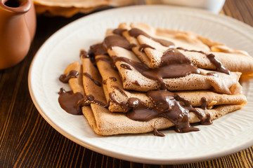 the chocolate pancakes watered with chocolate sauce in a plate on a table, selective focus © murziknata