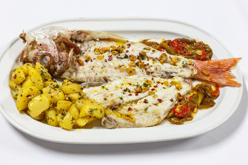 Delicious gourmet plate: cooked fish served with potatoes and vegetables isolated on white