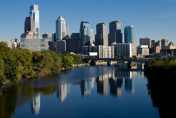 The skyline of Philidelphia. The Schuylkill river is in the foreground. The tallest buildings are on the left side. The buildings are reflected in the surface of the river. 
