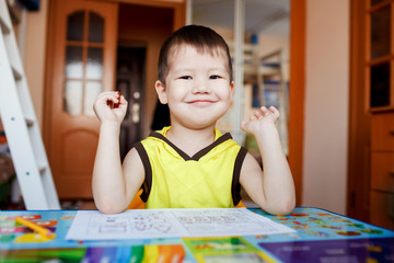 Little boy happy sitting at table after drawing, pre-school home education.