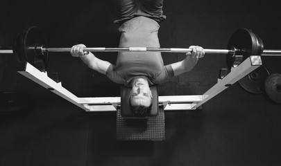 Muscular man lifting a barbell on bench at gym, top view