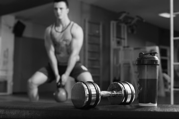 Whey protein, dumbbell and plastic shaker on gym floor