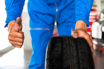 Mechanic holding a car wheel with thumb up sign in car garage se