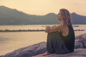 beautiful young woman sitting on the rocks by the sea and watchi