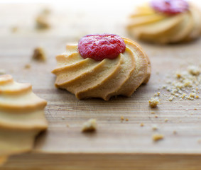 Sweet cookies with red fruit jam filling laying on wood table background with biscuit crumbs