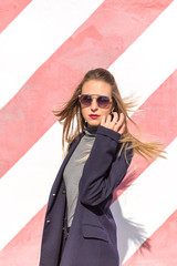 Fashion  girl posing over Red white striped wall background. Beauty woman with pink lips make-up posing on the street.
