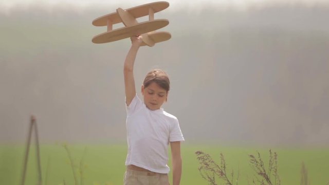 Caucasian boy playing with a model airplane. Portrait of a child with a wooden plane in a field.
