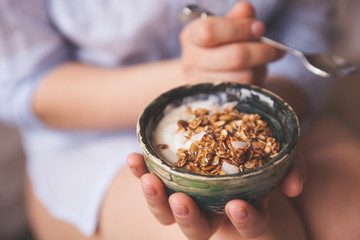 Young woman with muesli bowl. Girl eating breakfast cereals with nuts, pumpkin seeds, oats and yogurt in bowl. Girl holding homemade granola. Healthy snack or breakfst in the morning. - obrazy, fototapety, plakaty