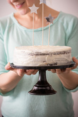 Woman's hands holding delicious homemade birthday white cake decorated with stars. Light blue background. Baking at home for events. Cooking sweet cake for holidays.