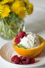 Vanilla Icecream with raspberry, summer dessert.  Delicious sundae scoop in an orange half on a white plate. Tasty sweet dessert for summer. Serving ice cream. Serving of refreshing tropical dessert