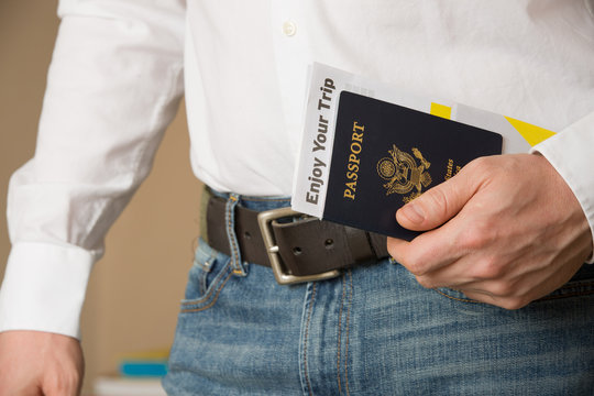 Image of a persons hand holding American passport and ready to travel. Man in a white shirt and jeans holding U.S. passport.