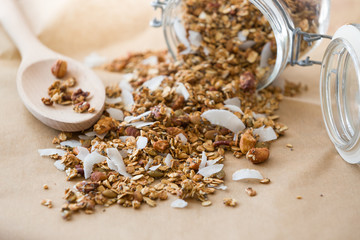 Glass jar of homemade organic granola with coconut and pecans on the baking paper background. Delicious breakfast cereal. Healthy muesli.