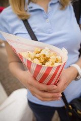 Blond woman in a blue t-shirt with striped paper bag full of popcorn. Girl holding and eating sweet popcorn