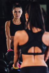 Fototapeta na wymiar Young woman choosing dumbbells in gym