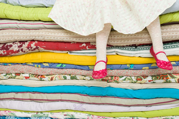 Legs of a little girl sitting on a pile of colorful mattresses. Decorations for the fairy tale 