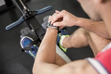 Muscular man on rowing machine using smart watch