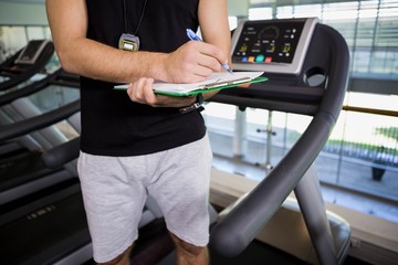 Mid section of man on treadmill writing on clipboard