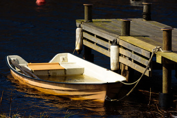 Obraz premium Orange plastic rowboat filled with water moored at a wooden pier in spring.