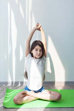 little girl doing gymnastics on a green mat for yoga. lotus Pose. children's fitness, yoga for children. doing fitness exercise and stretching in a bright room