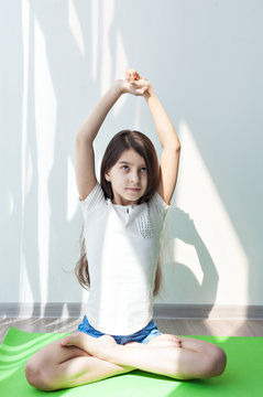 lotus Pose. little girl doing gymnastics on a green mat for yoga. doing fitness exercise and stretching in a bright room. children's fitness, yoga for children. 