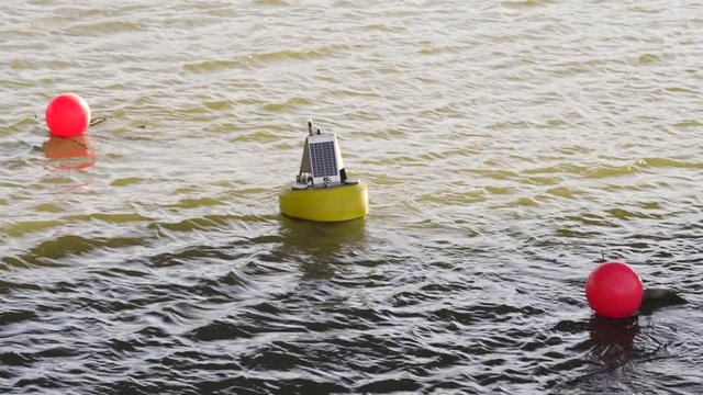A yellow buoy with solar panels on it and brightly colored floats by it.