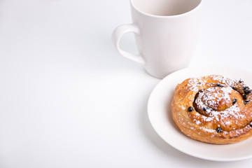 close up of sweet bun with raisins and cup over white