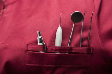  vari strumenti per dentista posti nella tasca di un camice amaranto quali lo specillo e lo...