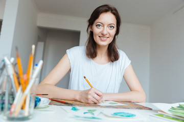 Happy beautiful woman artist drawing by pencil at the table